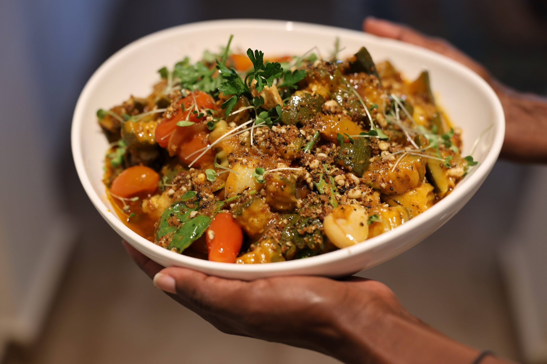 A vibrant bowl of slow-cooked vegetables, herbs and toasted spices held in two hands