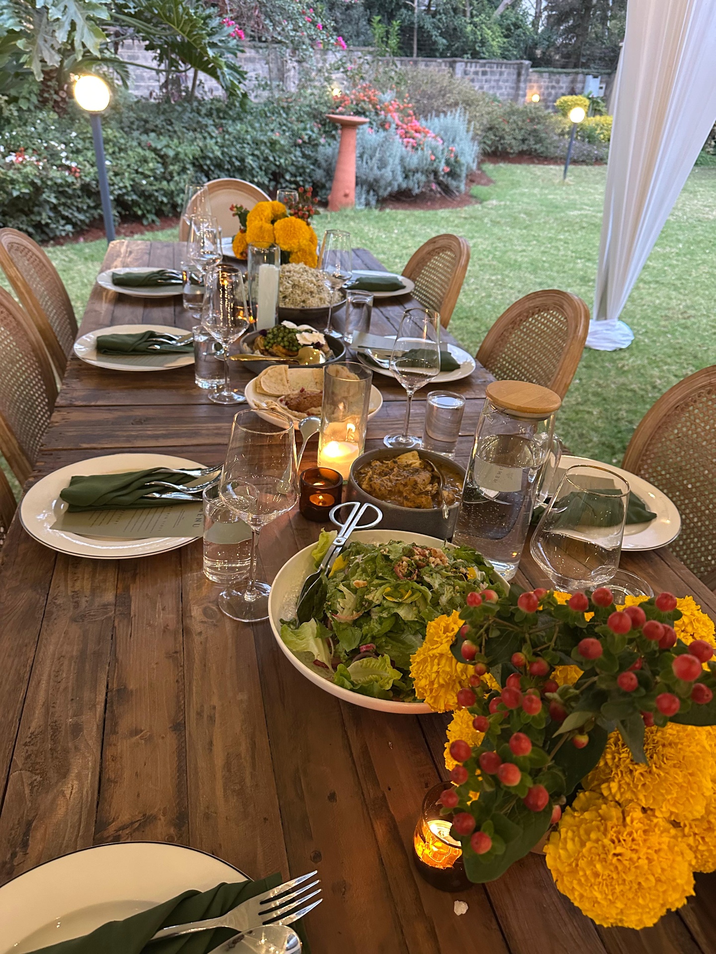 Long table dinner at dusk with shared platters, candles and marigolds